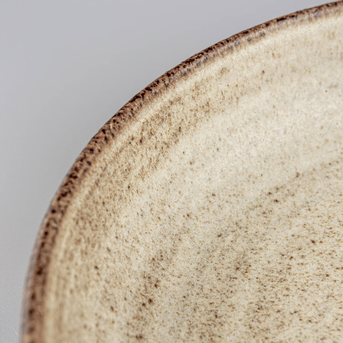 Interior of artisanal stoneware plate showing spiral wheel-thrown pattern and iron speckles.