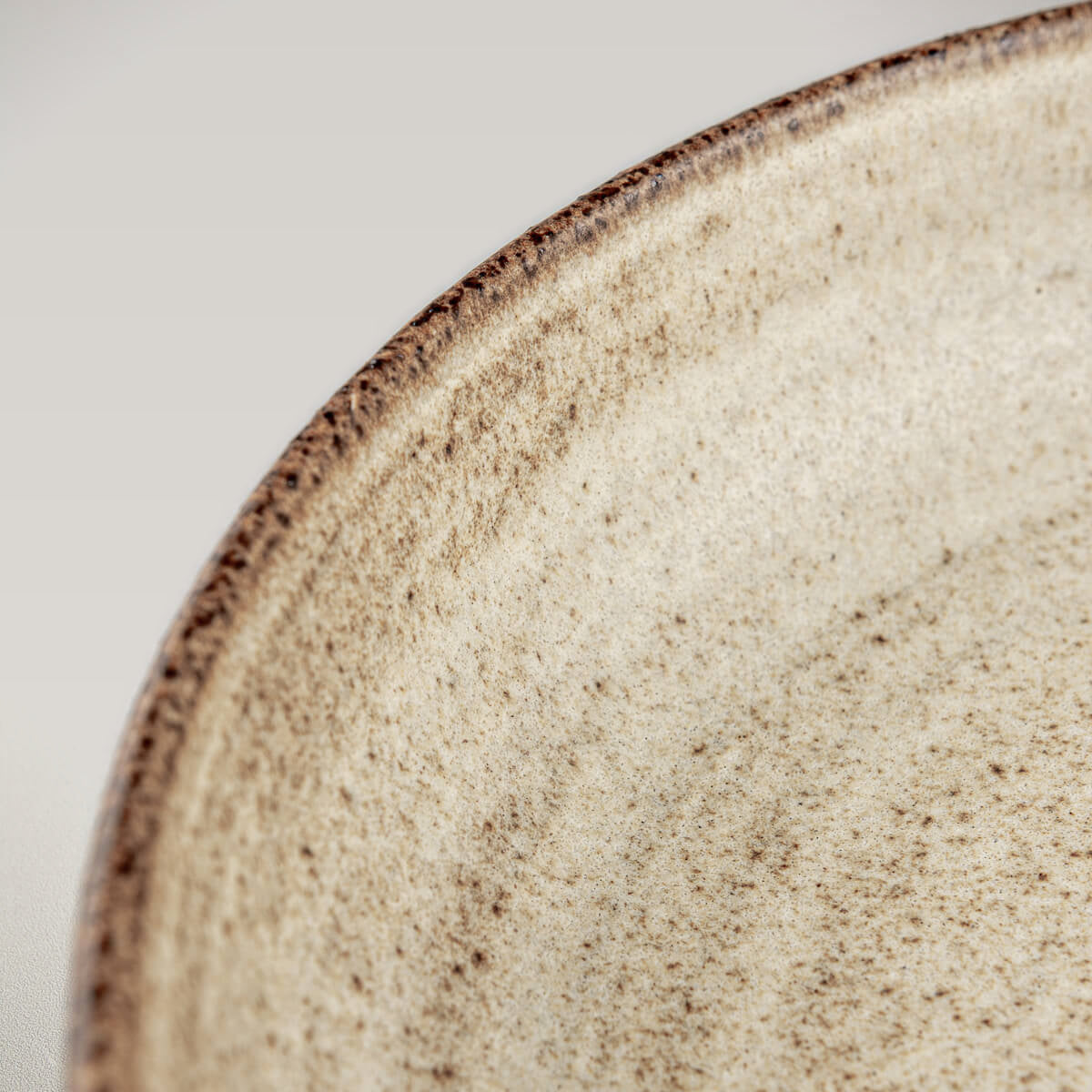 Interior of artisanal stoneware plate showing spiral wheel-thrown pattern and iron speckles.