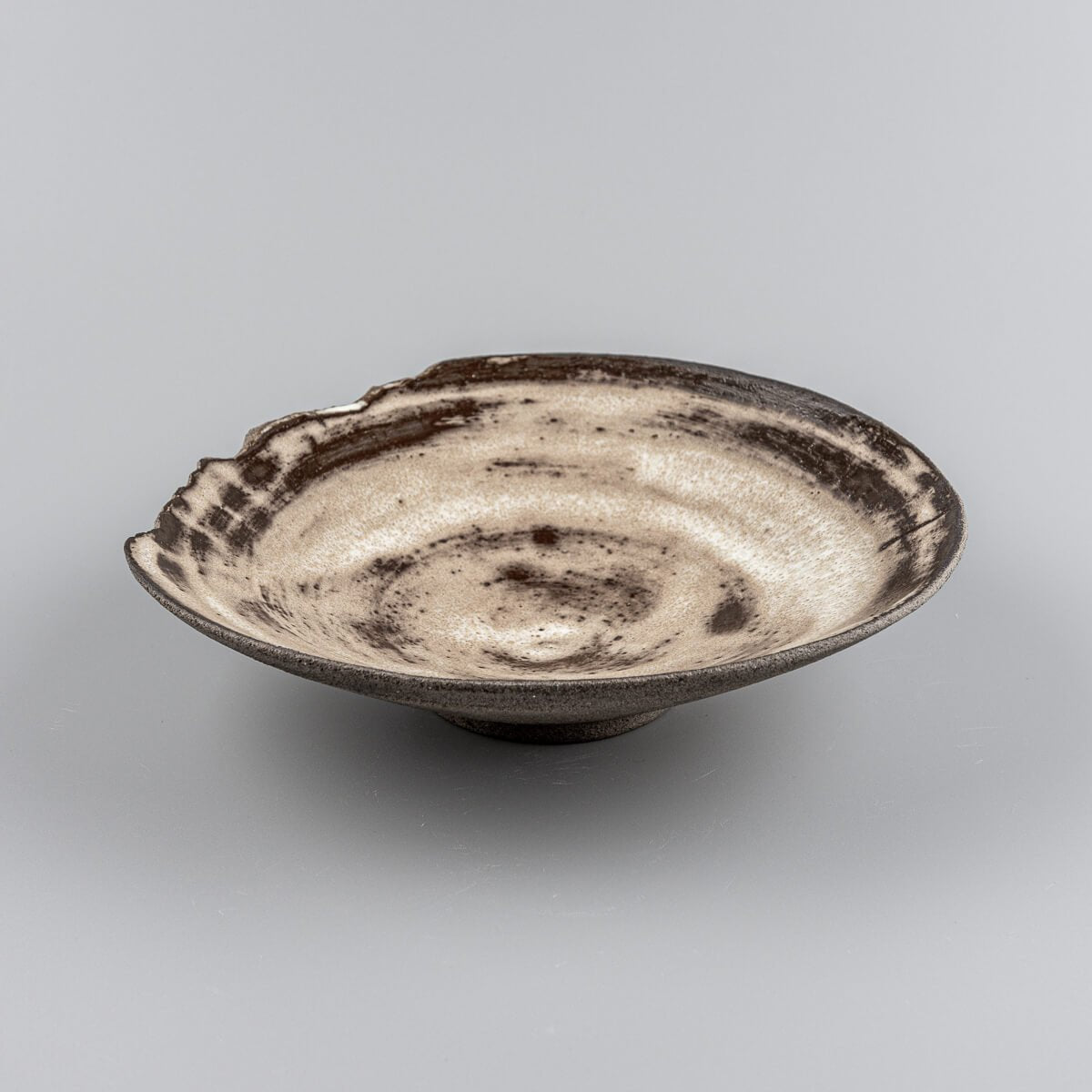 Rustic ceramic plate with matte glaze and textured chipped edge, perfect for handmade interior decor.