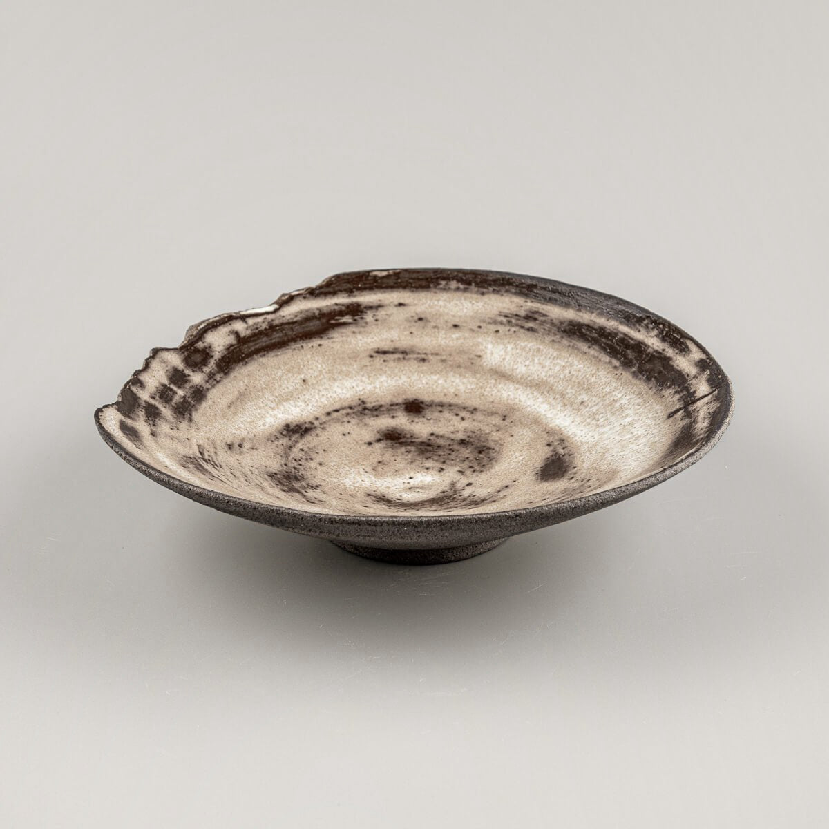 Rustic ceramic plate with matte glaze and textured chipped edge, perfect for handmade interior decor.