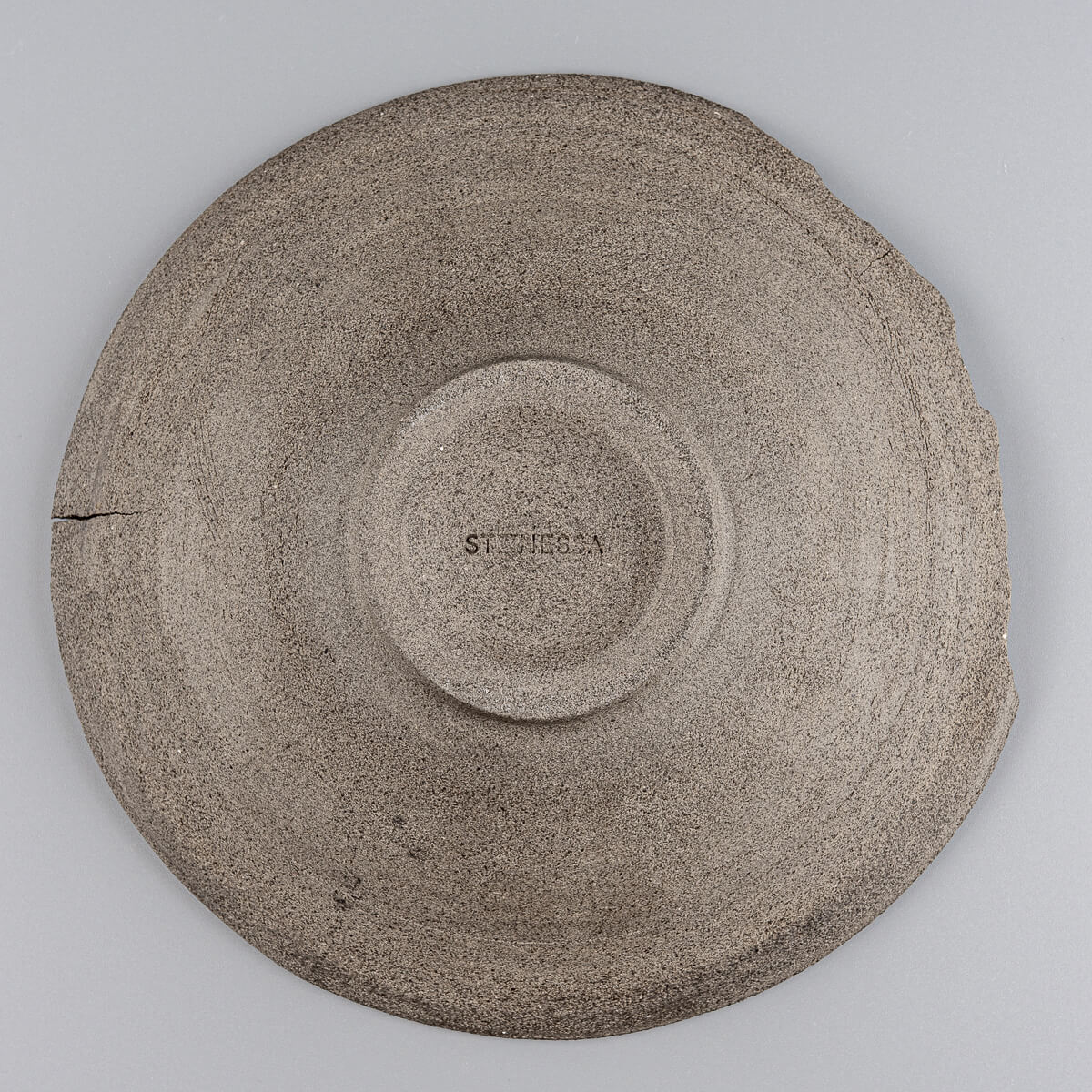 Underside of rustic ceramic plate revealing raw, unglazed dark stoneware.