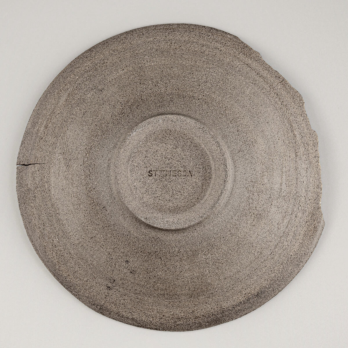 Underside of rustic ceramic plate revealing raw, unglazed dark stoneware.