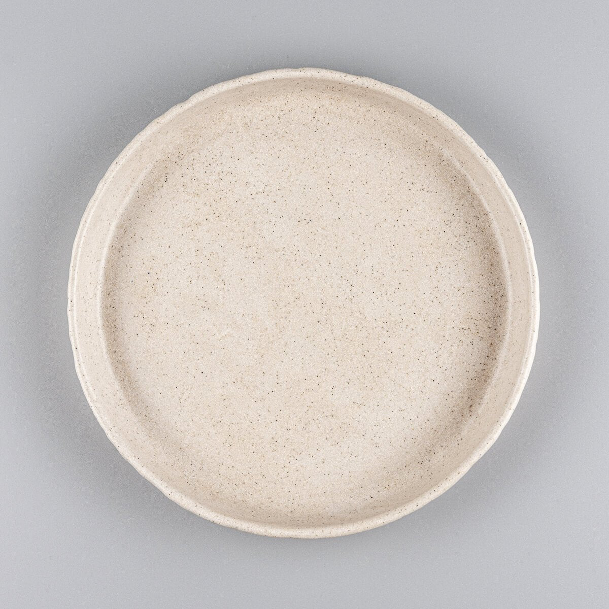 Small artisan stoneware dessert plate with matte beige glaze and hand-carved rim.