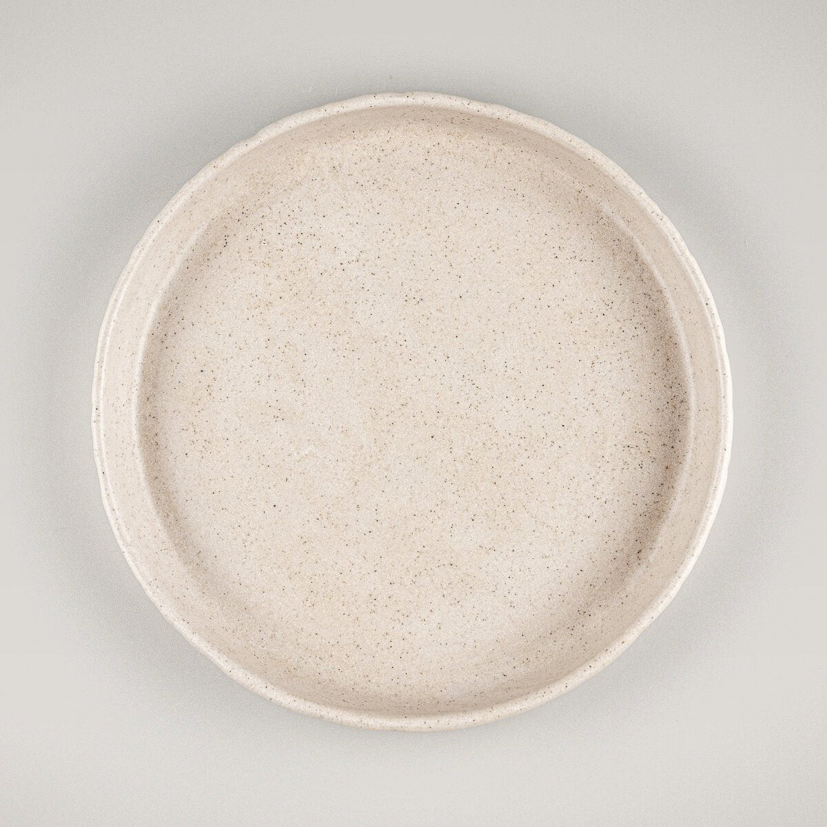 Small artisan stoneware dessert plate with matte beige glaze and hand-carved rim.
