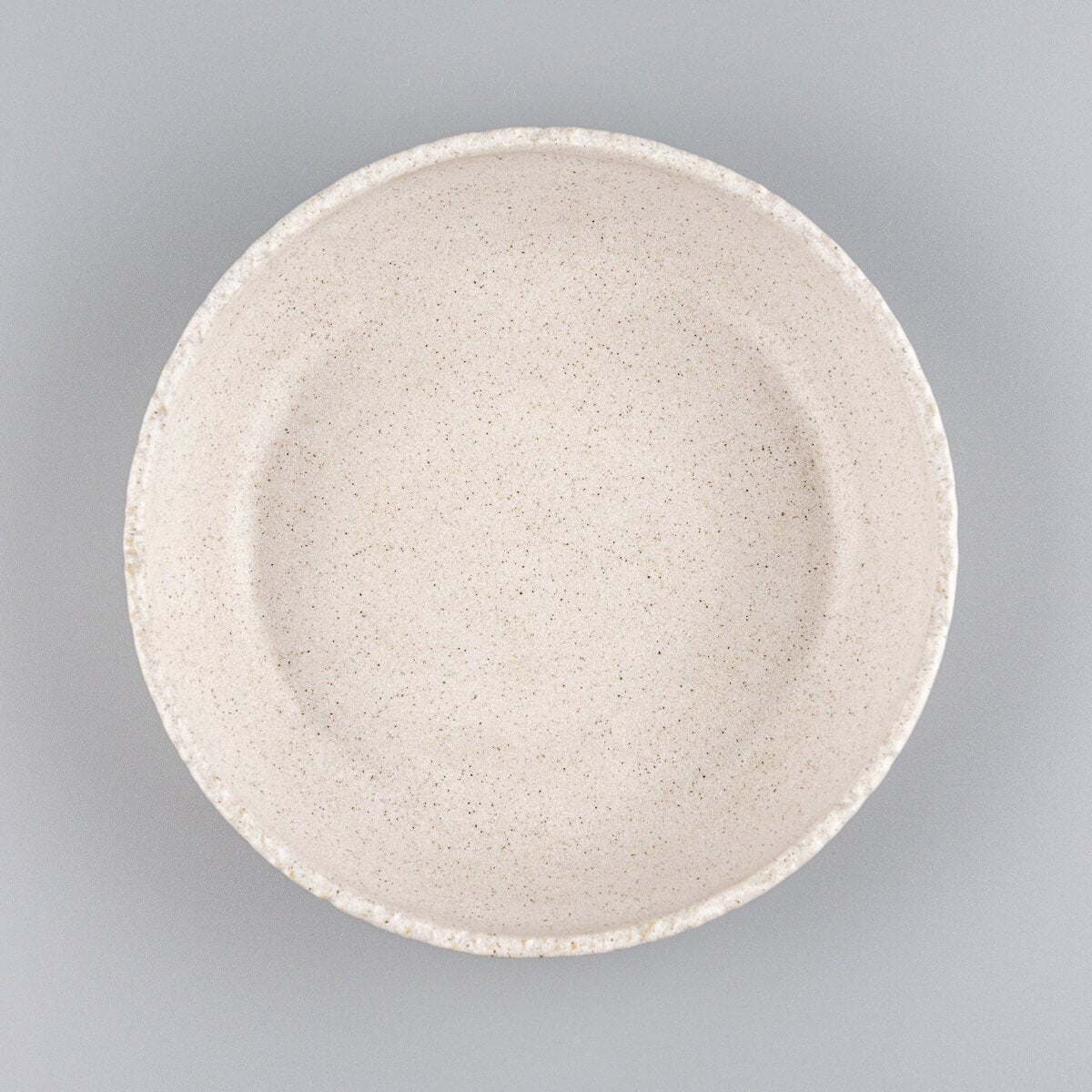 Stoneware dinner plate with matte beige glaze and artisan-carved rim, ideal for fine dining and interior design.