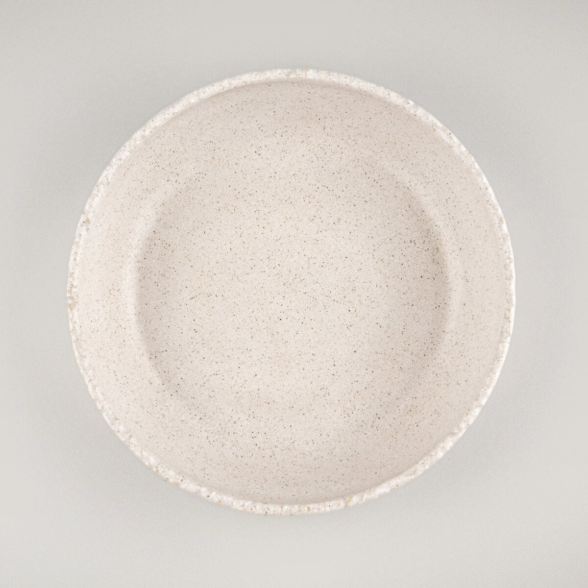 Stoneware dinner plate with matte beige glaze and artisan-carved rim, ideal for fine dining and interior design.