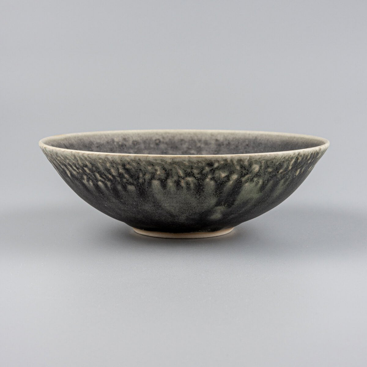 Side view of custom handcrafted ceramic bowl with matte green glaze and carved stoneware texture.