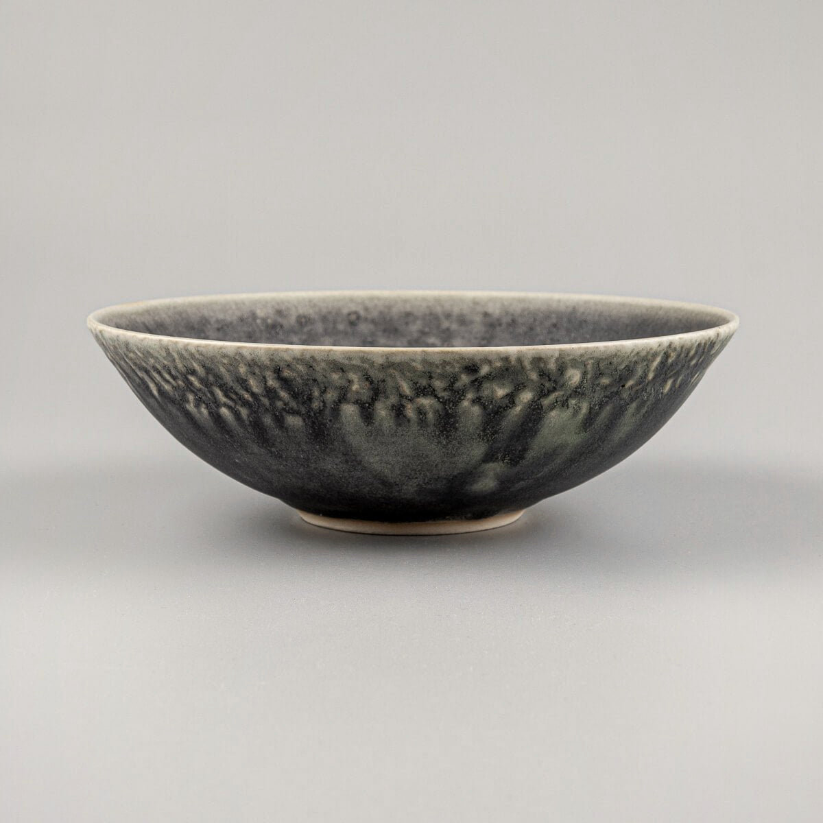Side view of custom handcrafted ceramic bowl with matte green glaze and carved stoneware texture.
