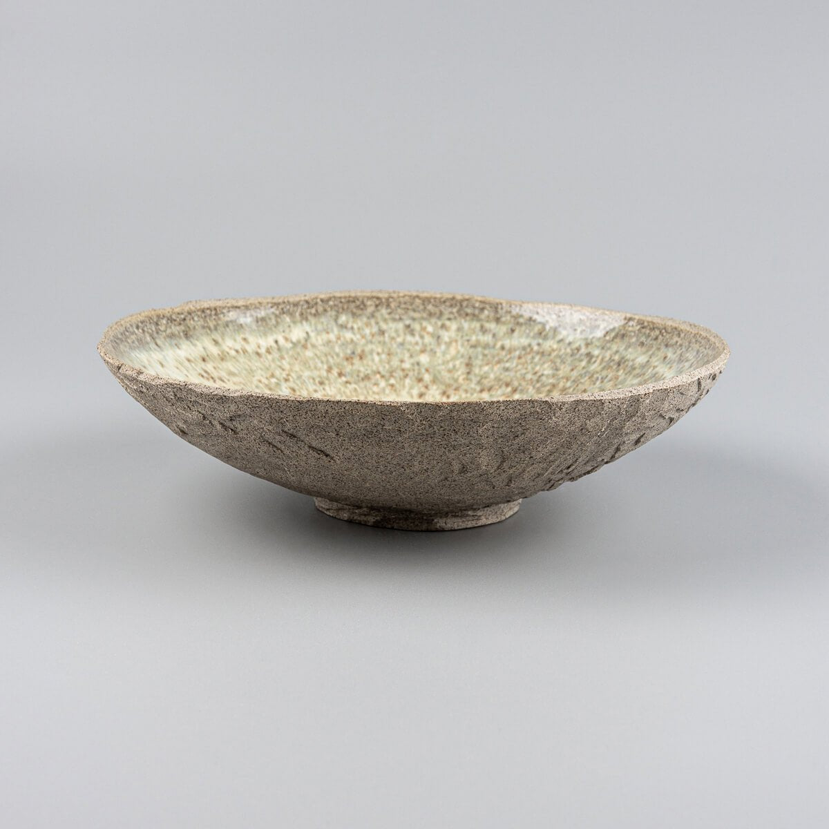 Side profile of artisanal ceramic plate with elevated base and rustic matte outer texture.