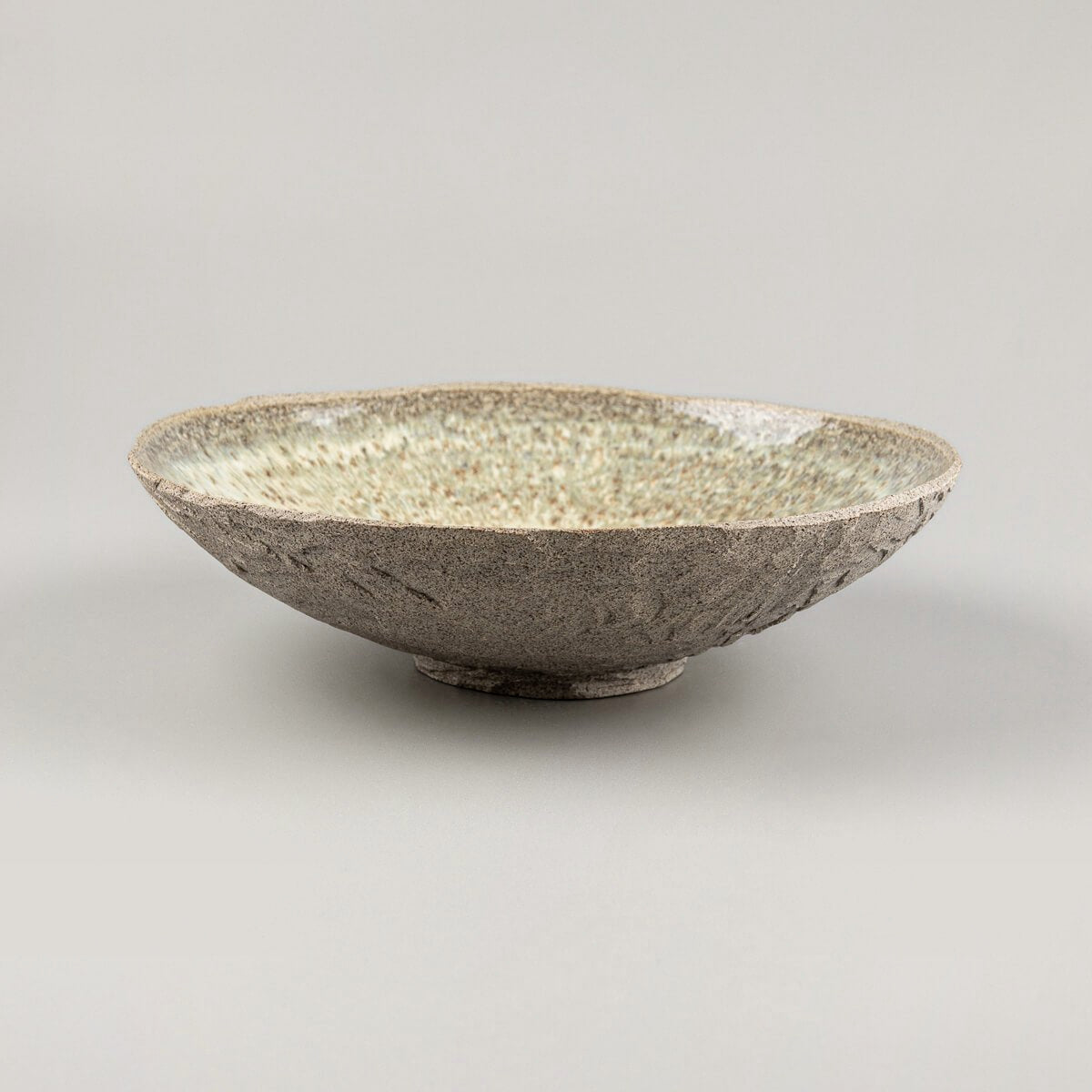 Side profile of artisanal ceramic plate with elevated base and rustic matte outer texture.