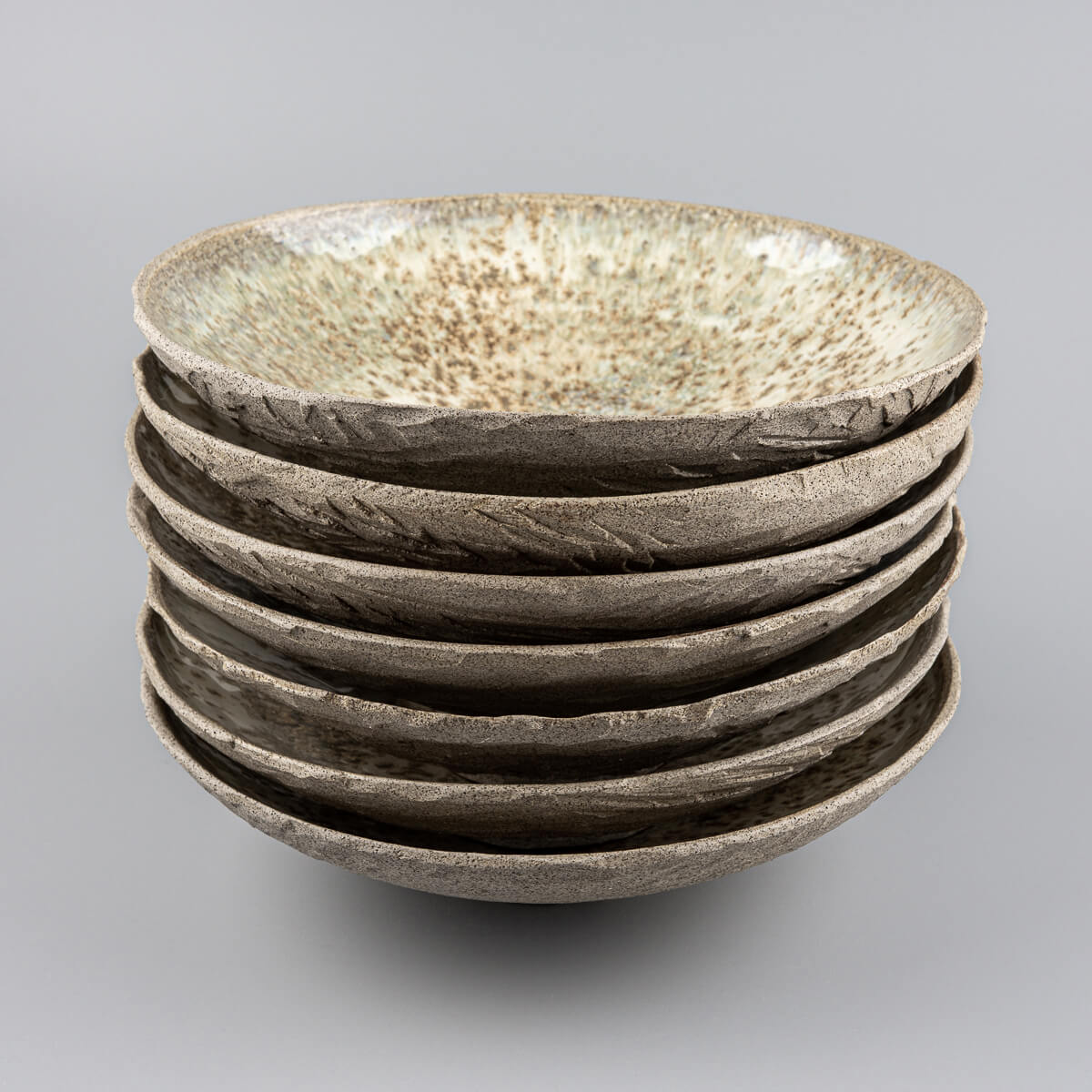 Top-down stack of handmade plates with textured exteriors and high-gloss interiors.