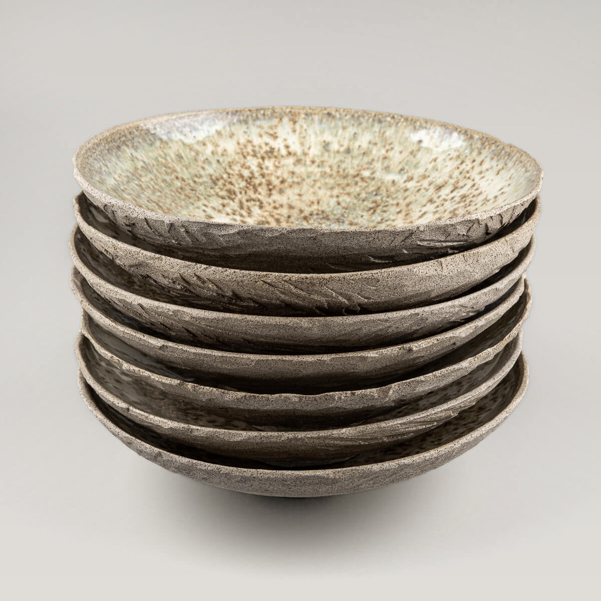 Top-down stack of handmade plates with textured exteriors and high-gloss interiors.