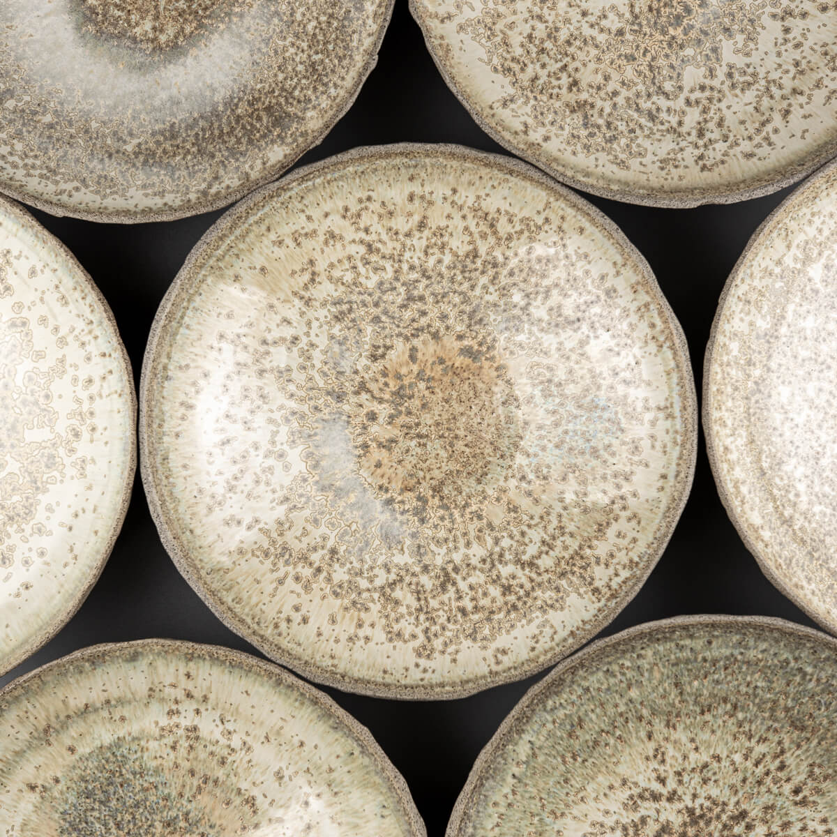 Grouped table setting of collectible handmade ceramic plates for restaurant or home use.