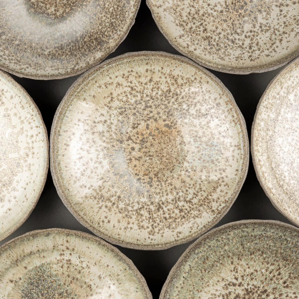 Grouped table setting of collectible handmade ceramic plates for restaurant or home use.