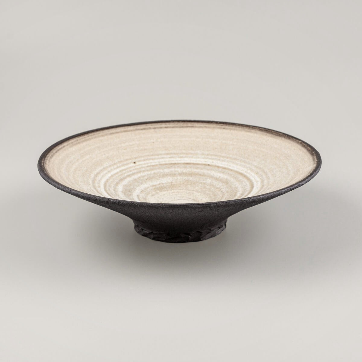 Sculptural ceramic plate with raw black clay exterior and minimalist design.