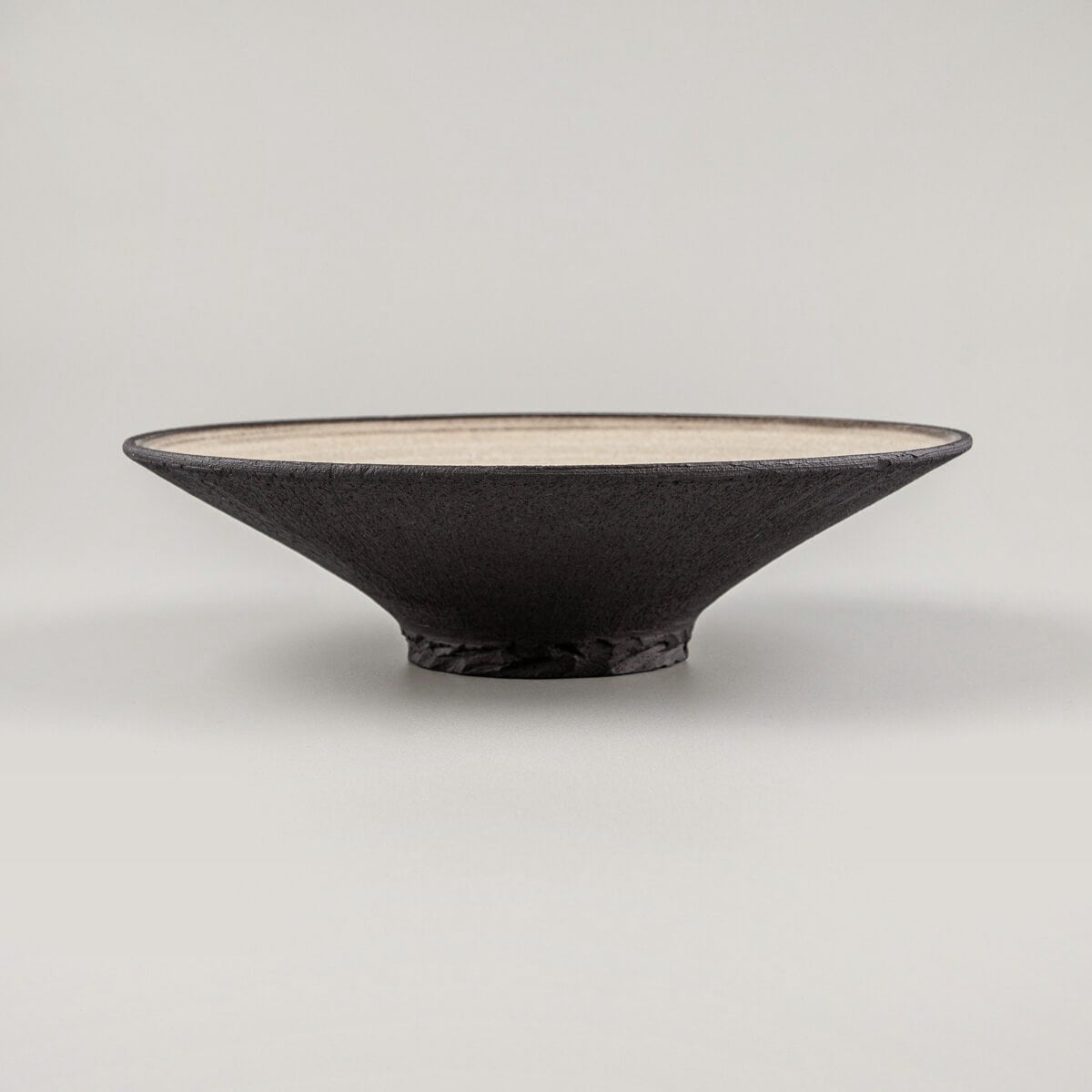 Profile of handcrafted ceramic plate with elevated foot and sharply beveled rim.
