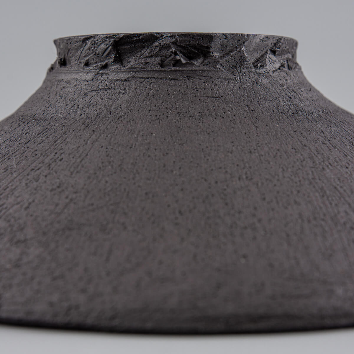 Underside of handcrafted plate showing unglazed black clay and artisanal wheel-thrown details.
