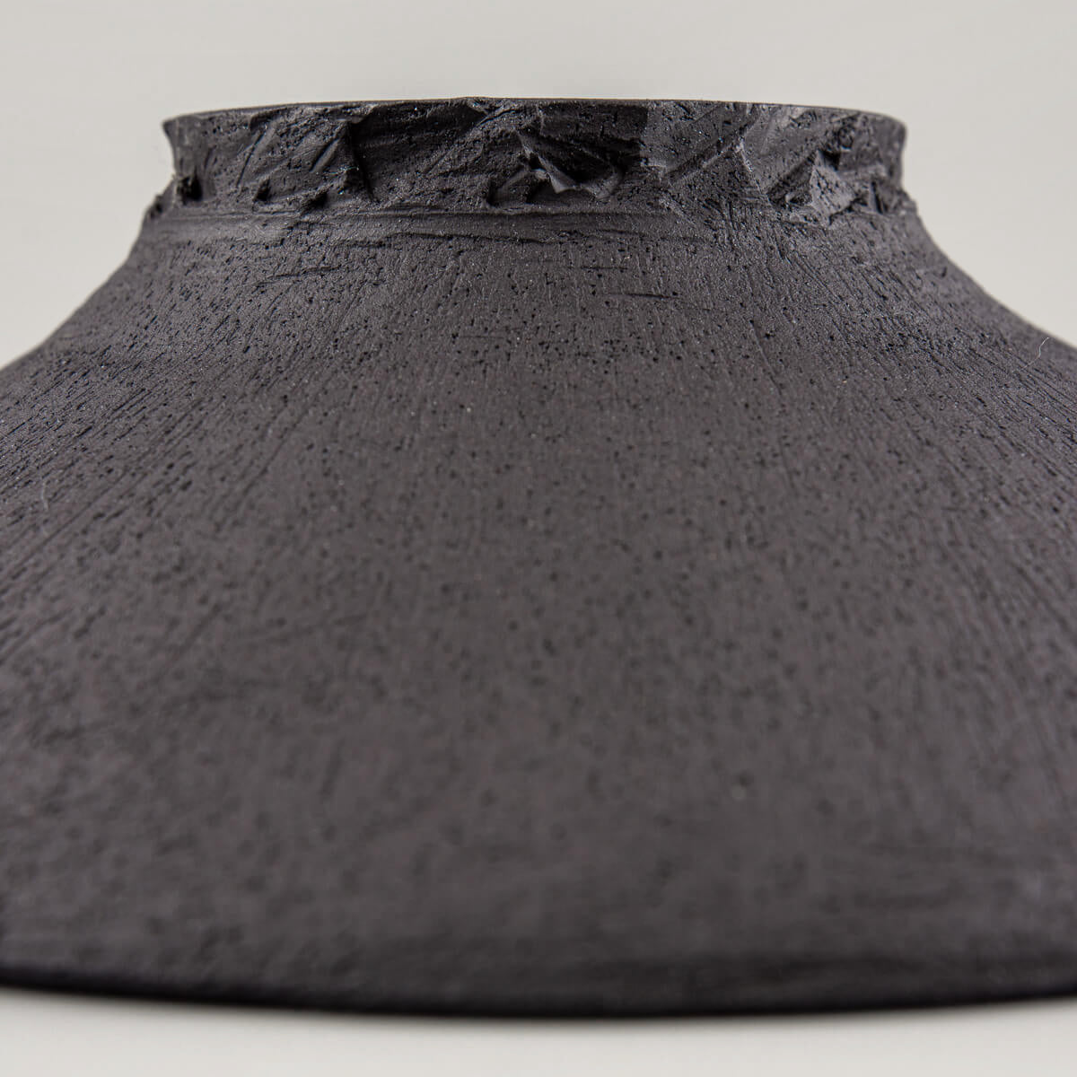 Underside of handcrafted plate showing unglazed black clay and artisanal wheel-thrown details.