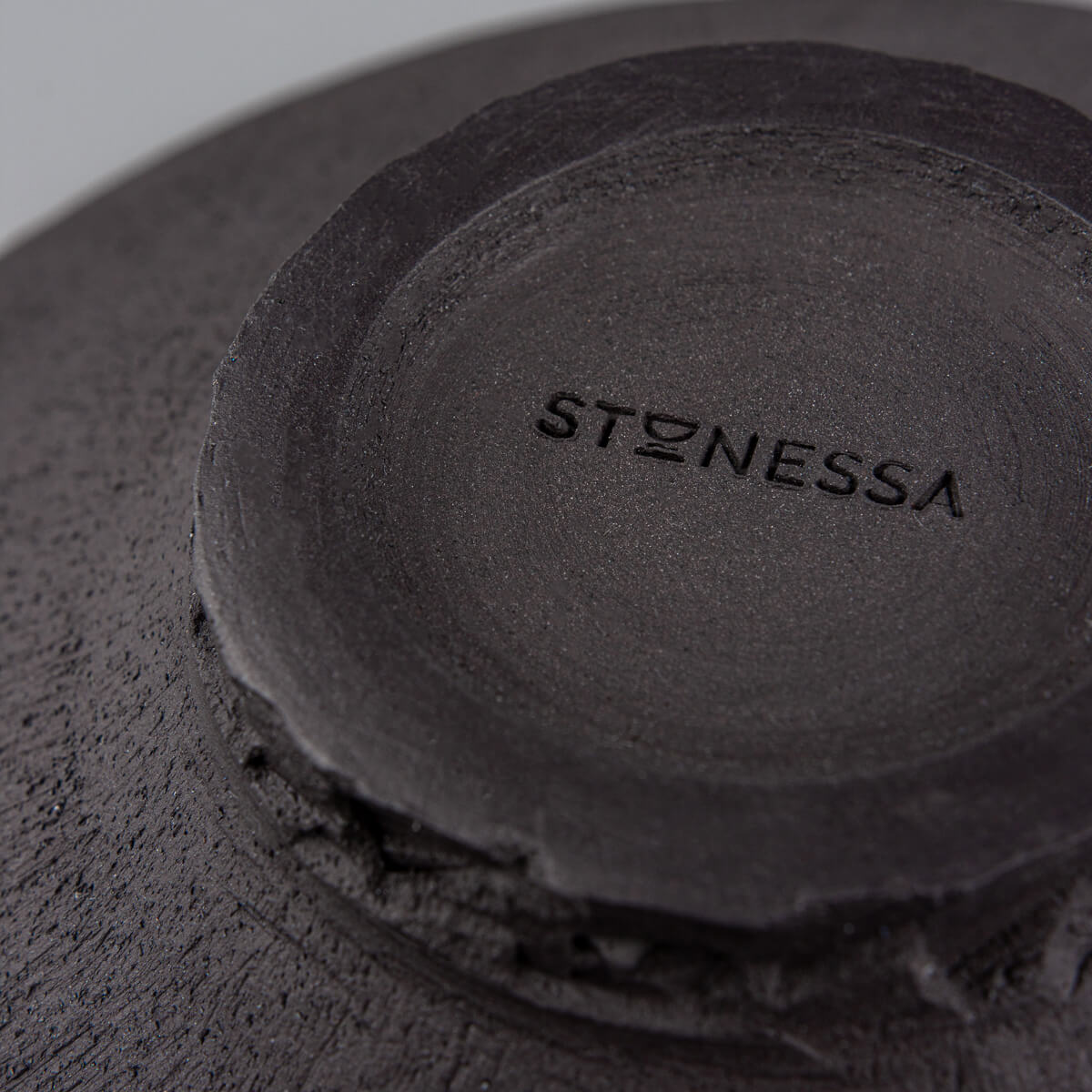 Underside of handcrafted plate showing unglazed black clay and artisanal wheel-thrown details.