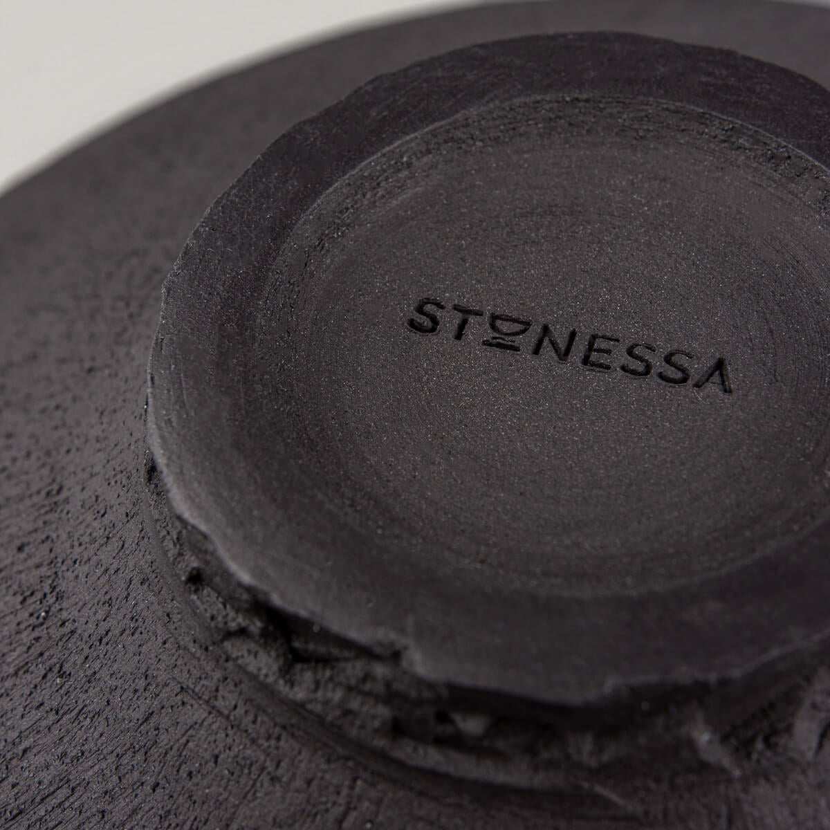 Underside of handcrafted plate showing unglazed black clay and artisanal wheel-thrown details.