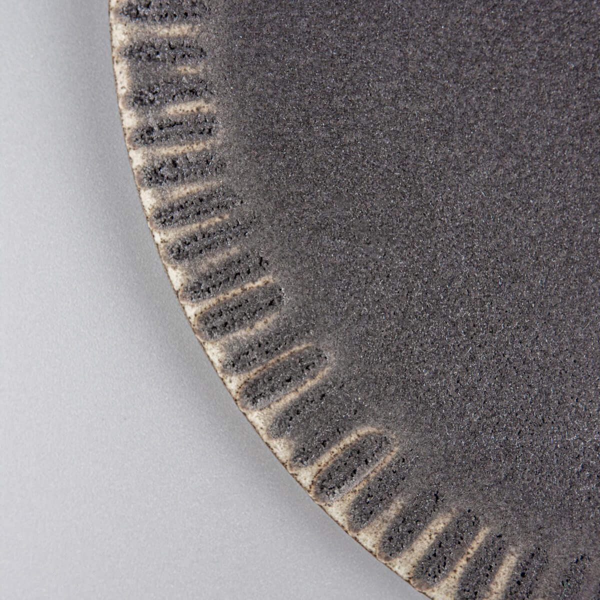 Close-up of textured rim on artisanal ceramic dessert plate for boutique hotel dining.
