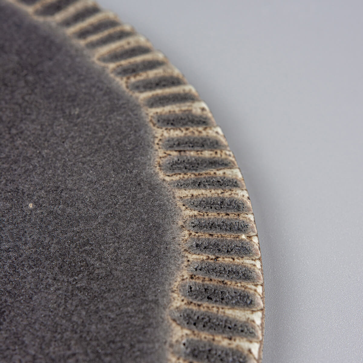Close-up of textured rim on handmade ceramic serving plate with matte dark glaze for desserts and fine dining.
