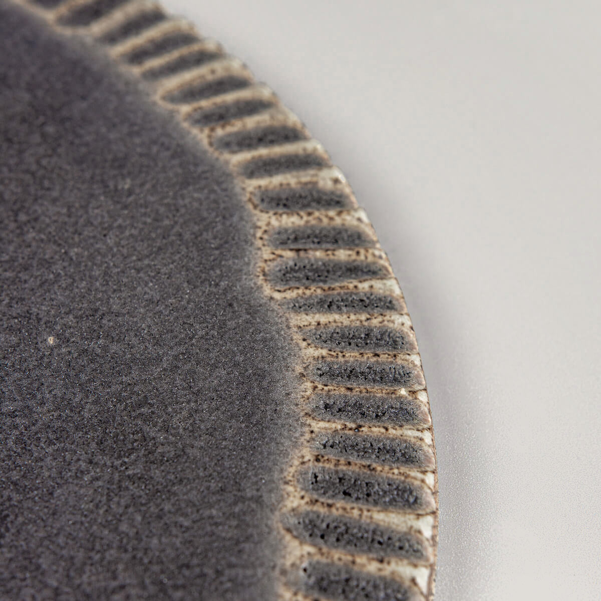 Close-up of textured rim on handmade ceramic serving plate with matte dark glaze for desserts and fine dining.
