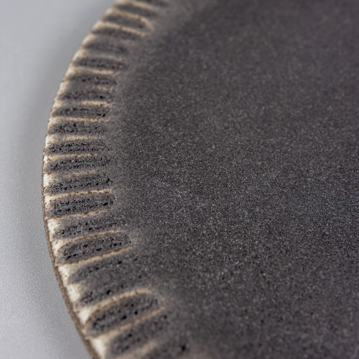 Detail of hand-shaped rim on dark stoneware ceramic plate for elegant food presentation.