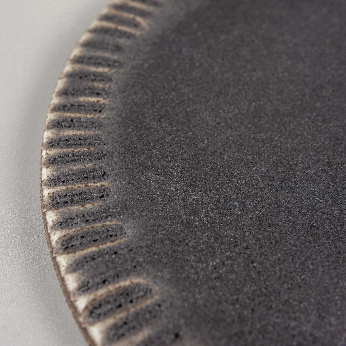 Detail of hand-shaped rim on dark stoneware ceramic plate for elegant food presentation.