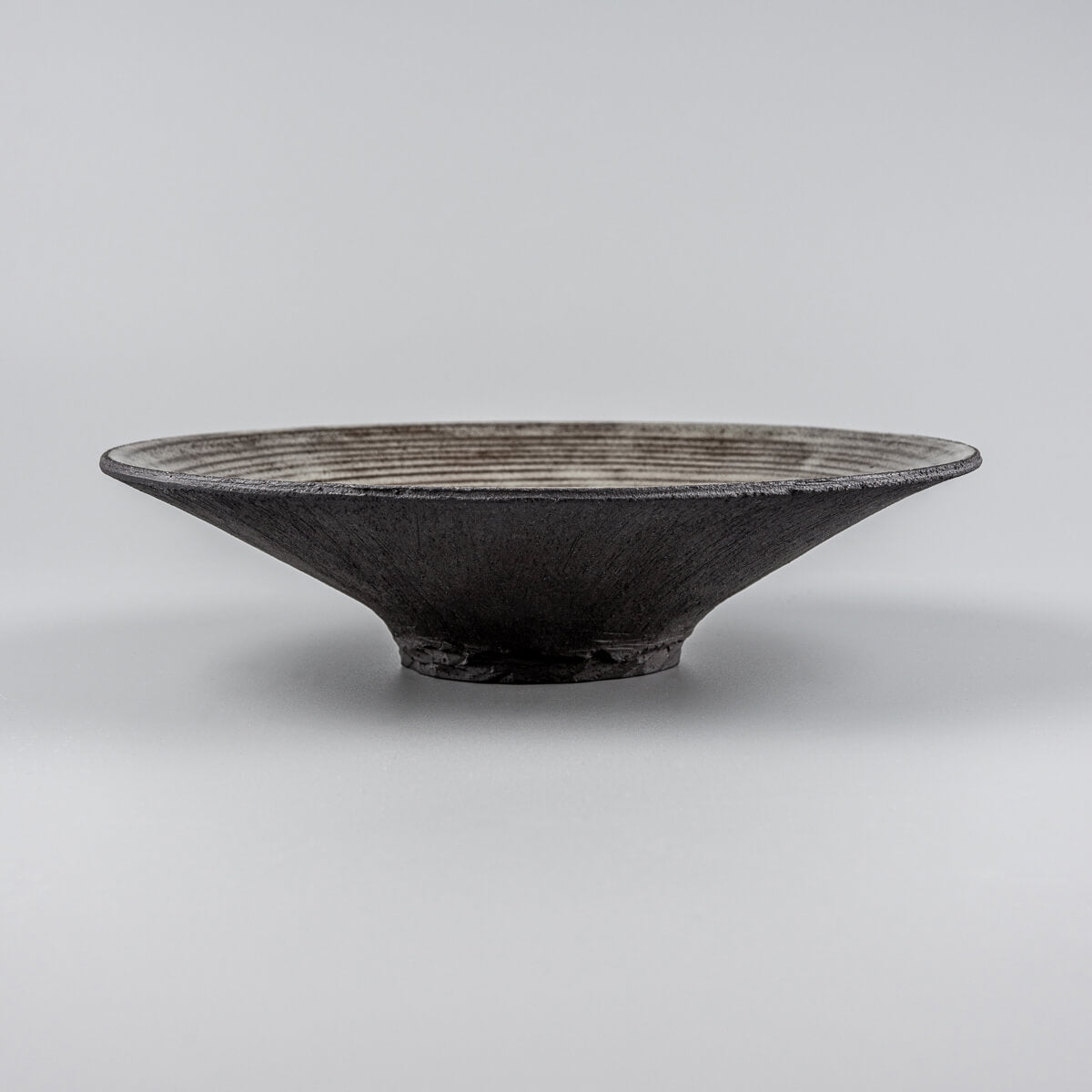 Side profile of stoneware dinner plate with elevated base for premium culinary presentation.