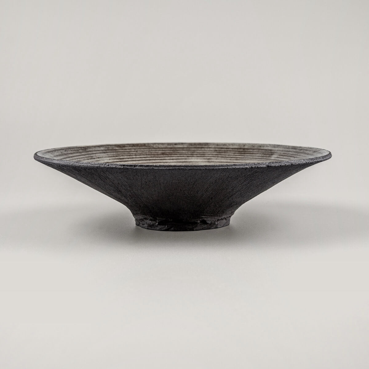 Side profile of stoneware dinner plate with elevated base for premium culinary presentation.