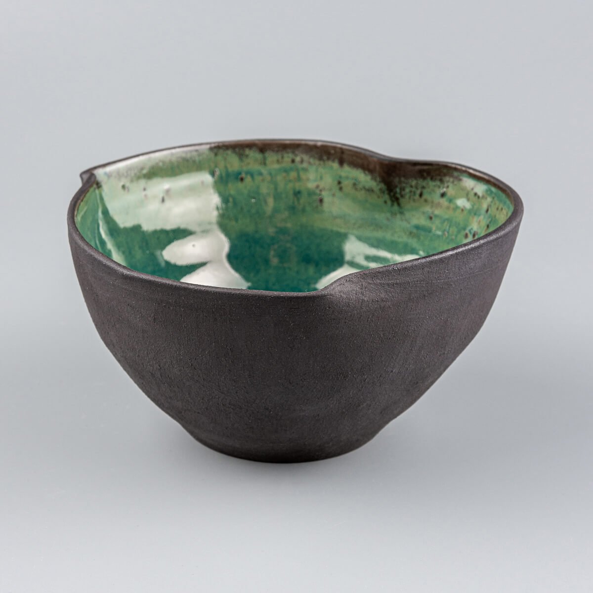 Front view of handmade stoneware bowl with sculpted rim and glossy green glazed interior.