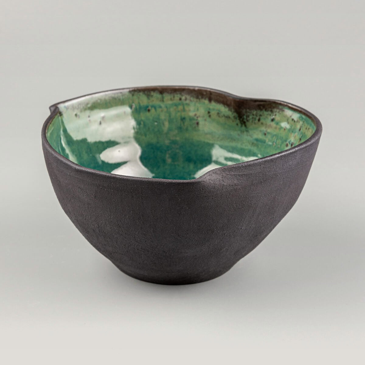 Front view of handmade stoneware bowl with sculpted rim and glossy green glazed interior.
