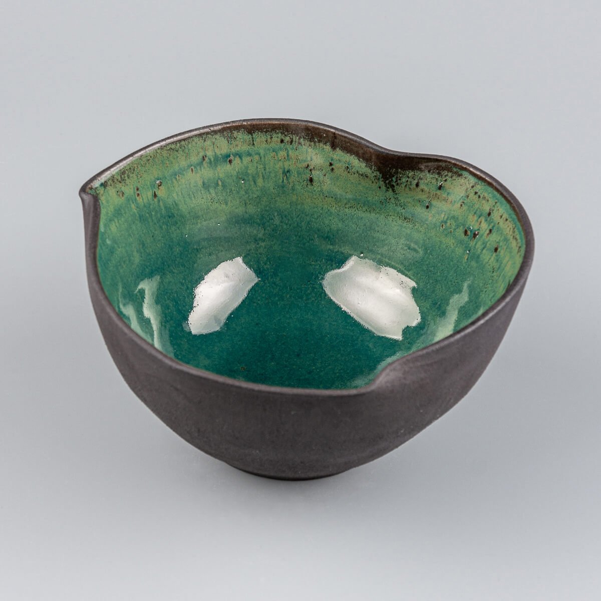 Angled top-down view of handmade pottery bowl showing irregular curved edges and reflective glaze.