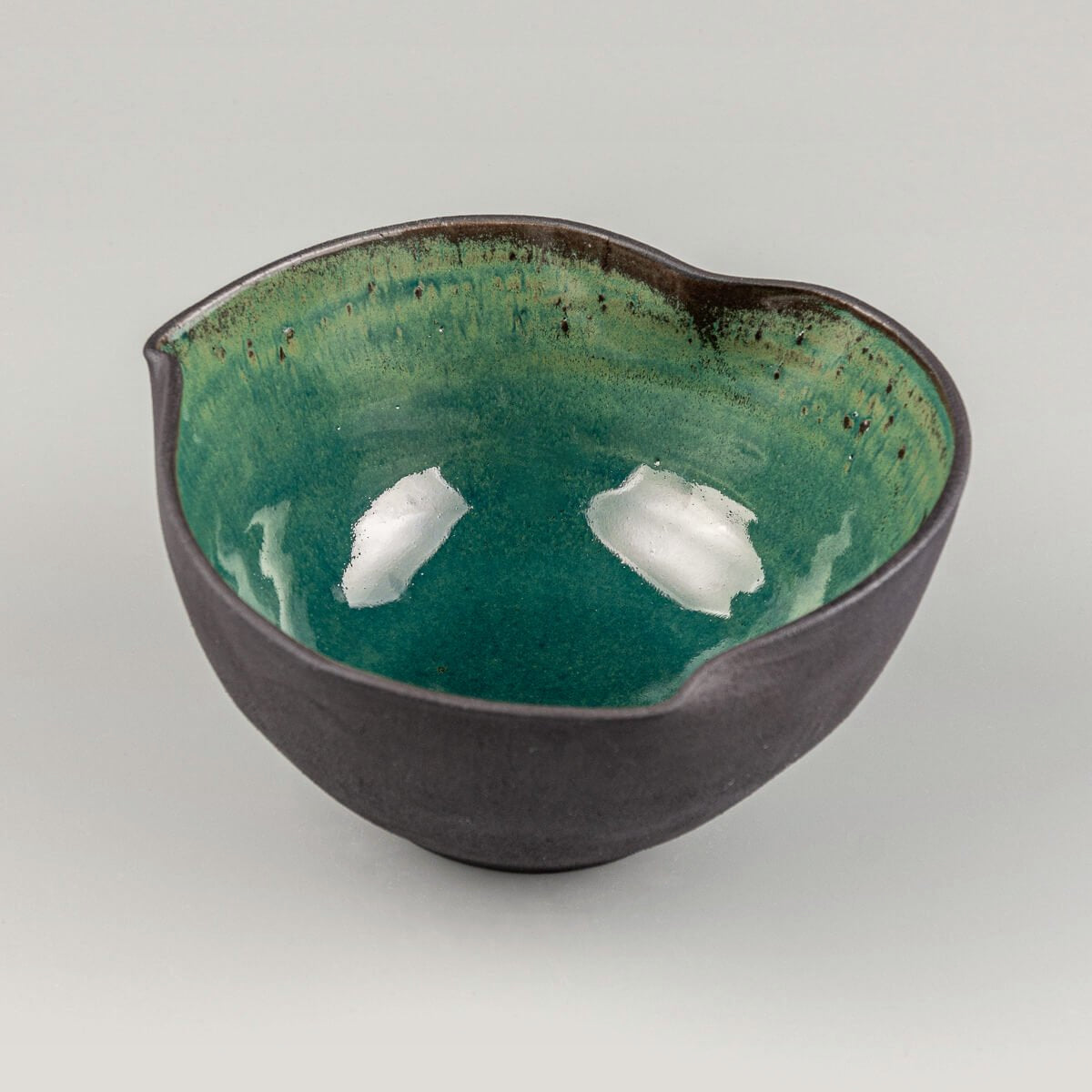 Angled top-down view of handmade pottery bowl showing irregular curved edges and reflective glaze.