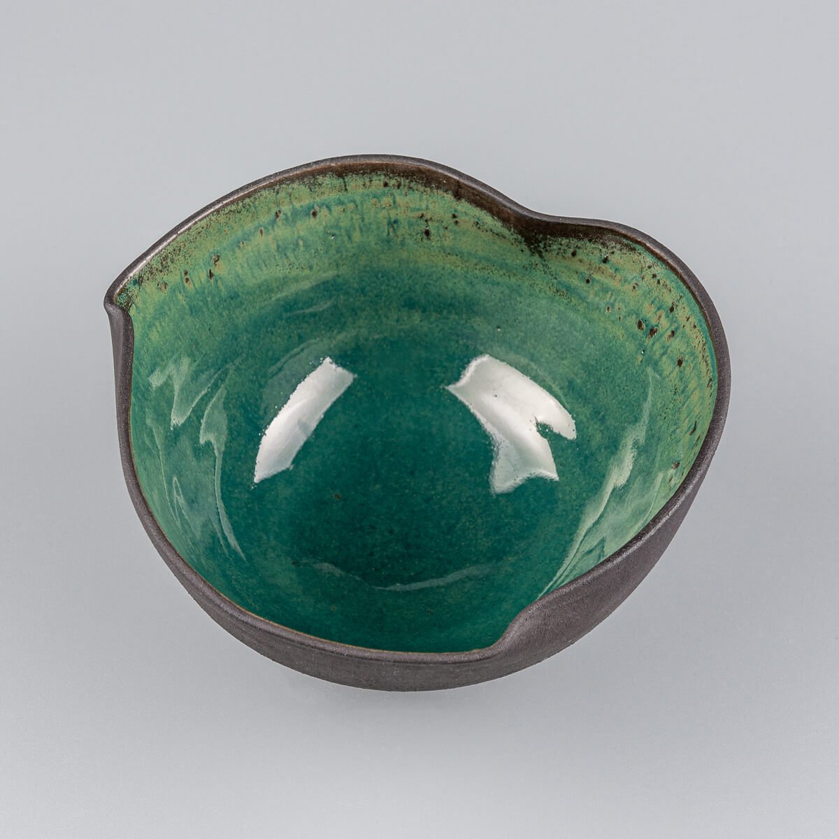 Interior detail of handcrafted ceramic bowl with rich green glaze and speckled finish.
