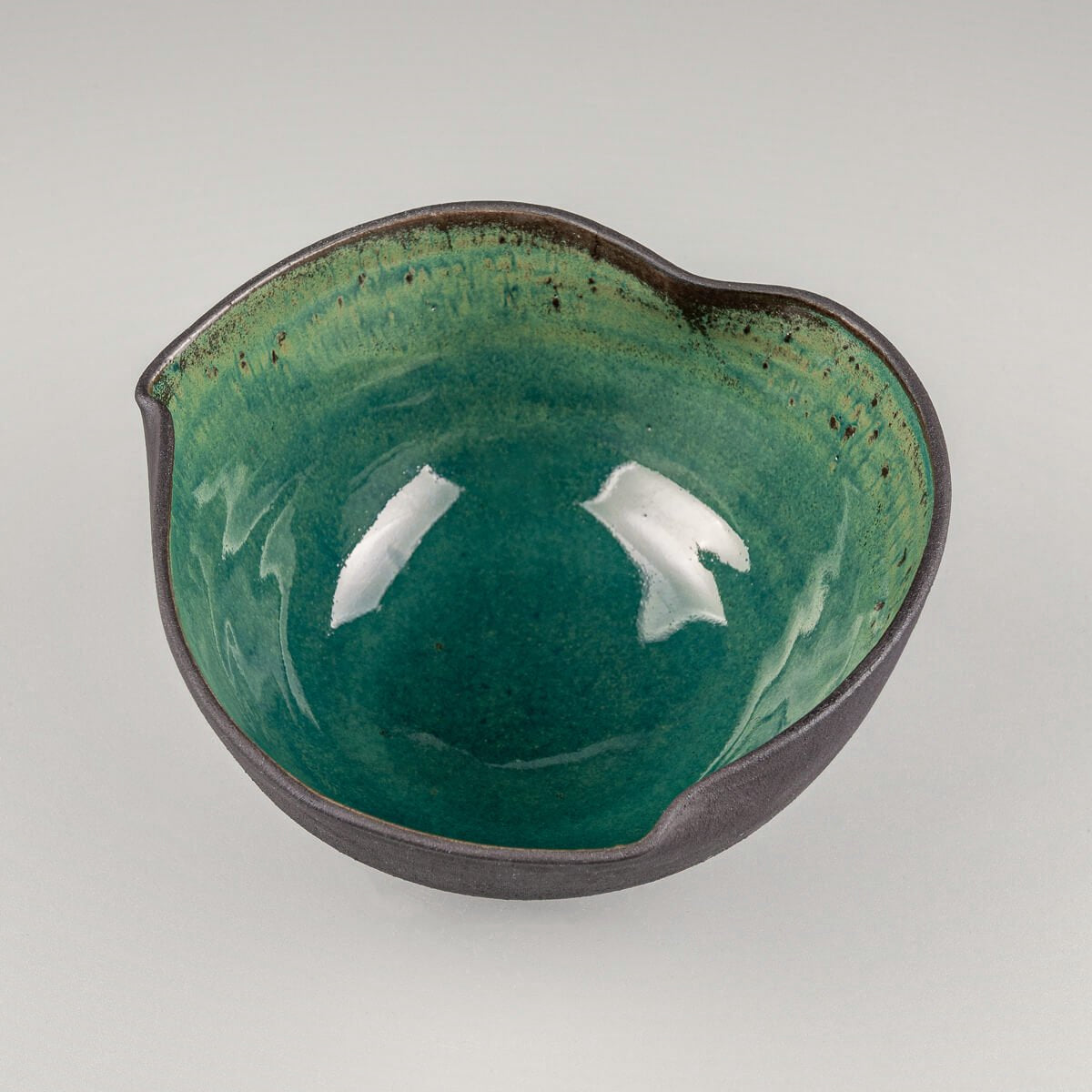 Interior detail of handcrafted ceramic bowl with rich green glaze and speckled finish.