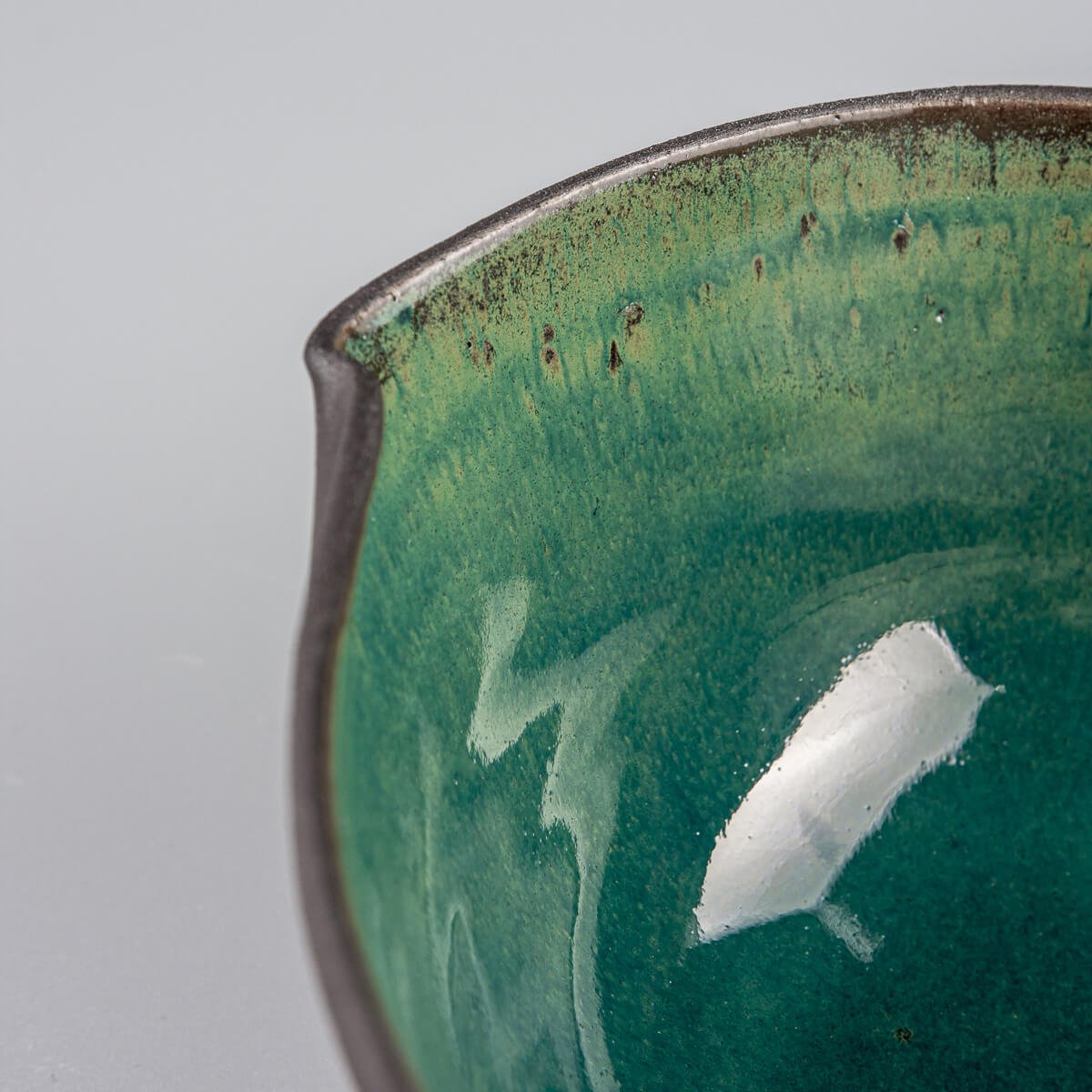 Interior texture of glazed ceramic bowl with emerald tones and artisan surface variations.