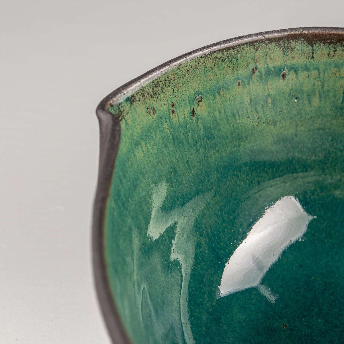 Interior texture of glazed ceramic bowl with emerald tones and artisan surface variations.