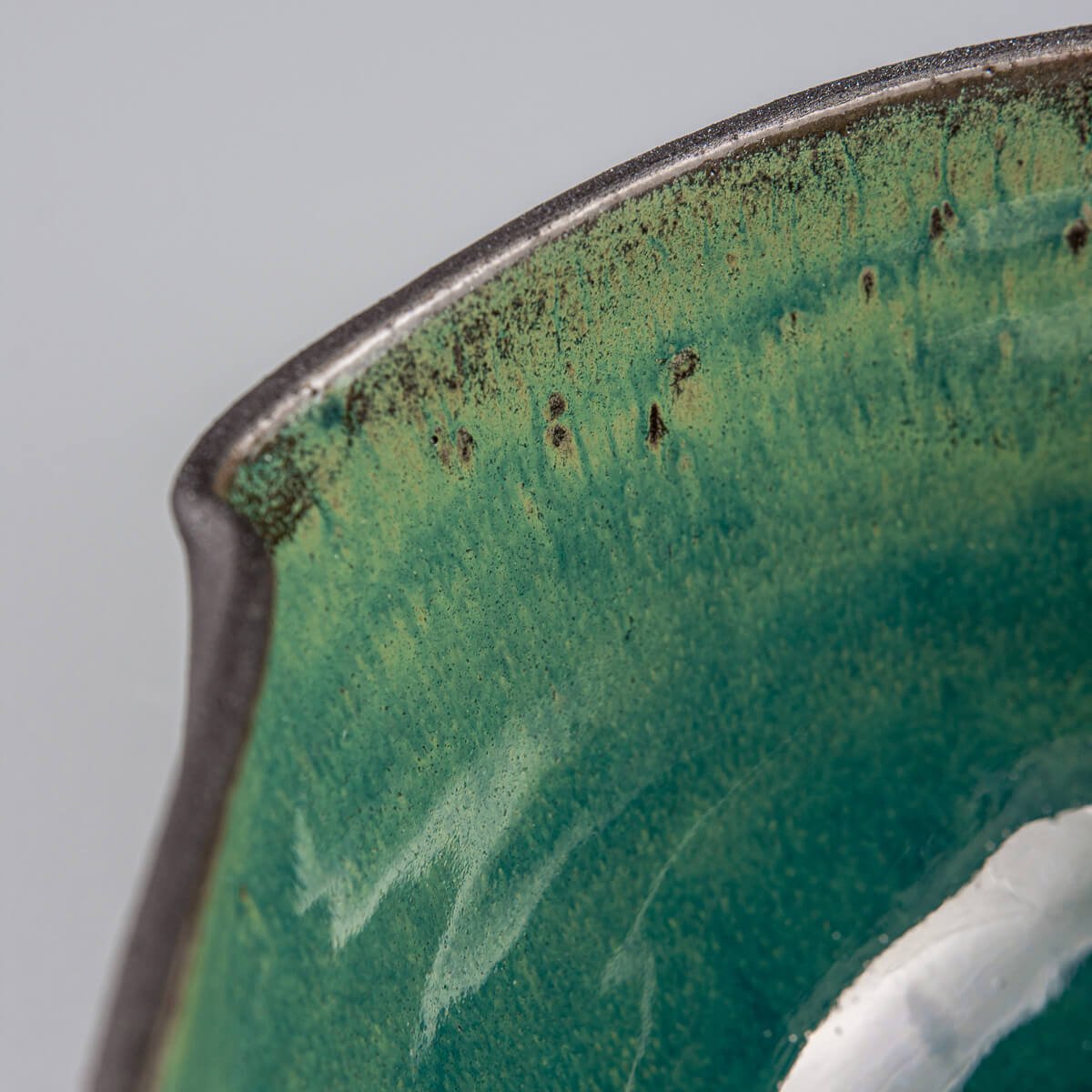 Macro view of inner rim and color depth of handmade green-glazed ceramic bowl.
