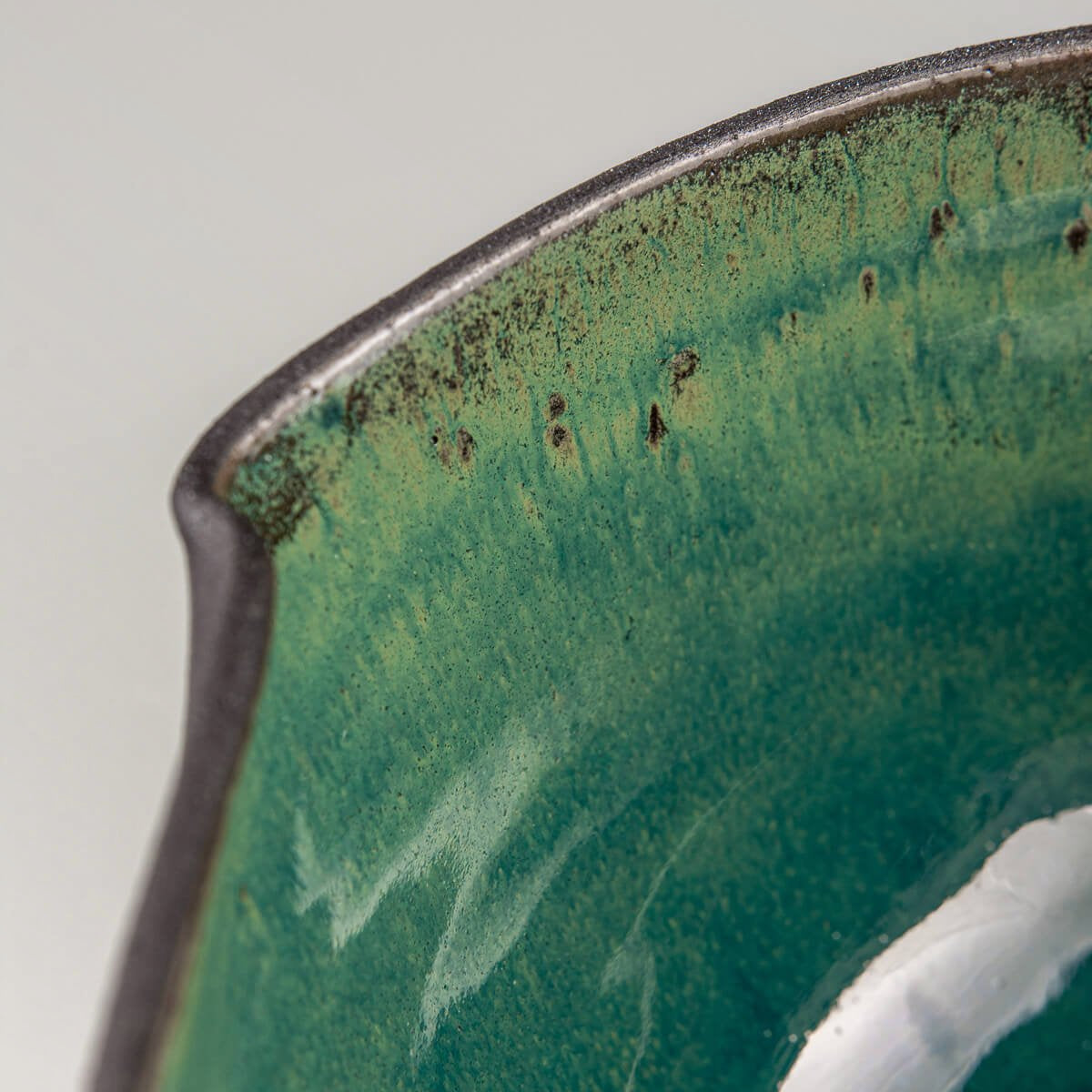 Macro view of inner rim and color depth of handmade green-glazed ceramic bowl.