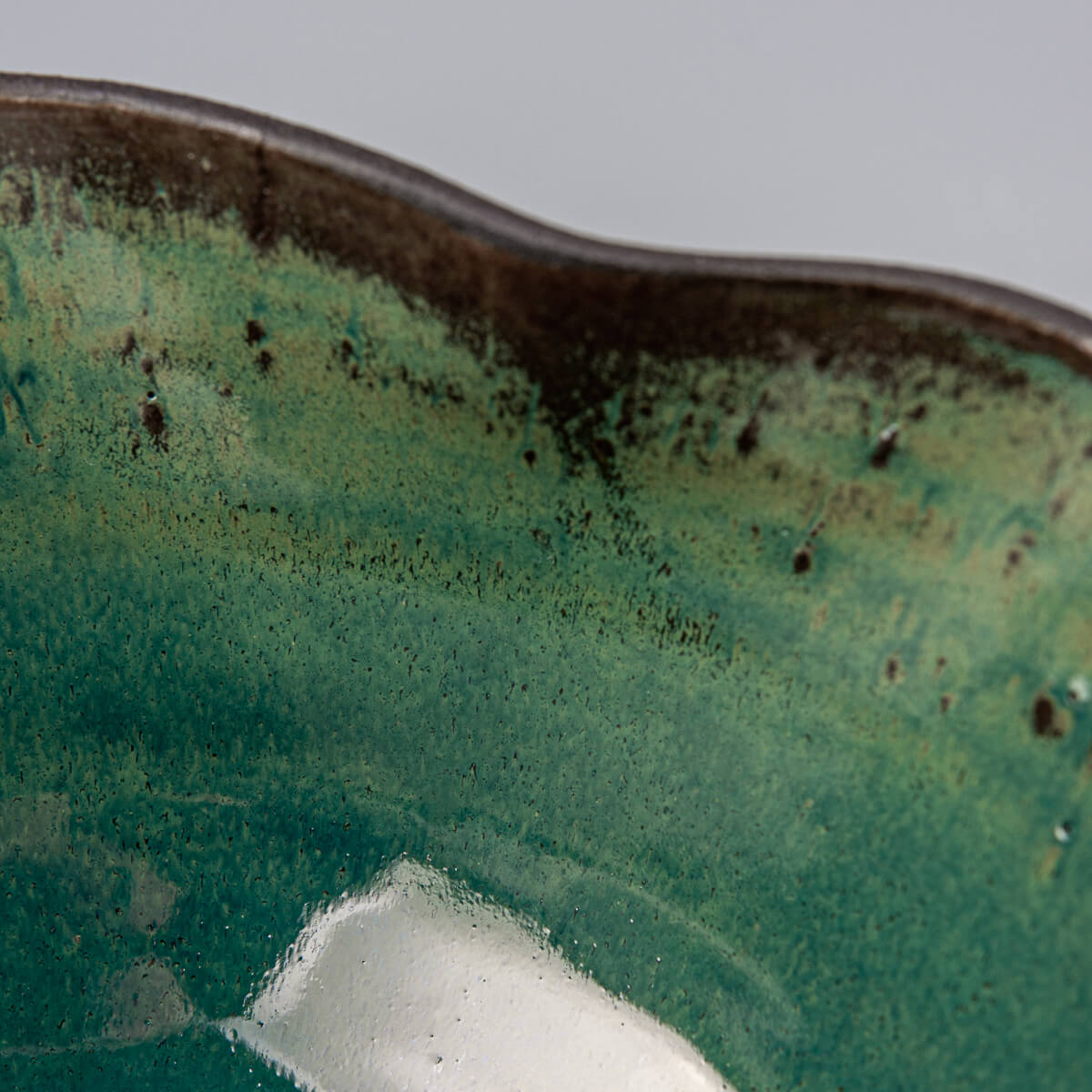 Interior detail of handcrafted ceramic bowl with rich green glaze and speckled finish.