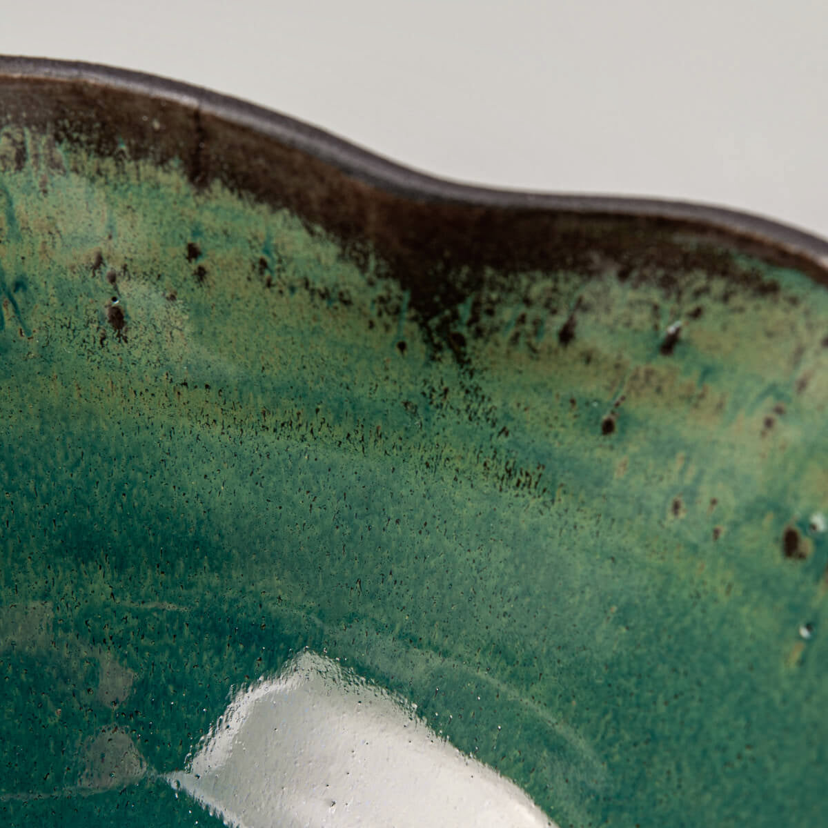 Interior detail of handcrafted ceramic bowl with rich green glaze and speckled finish.