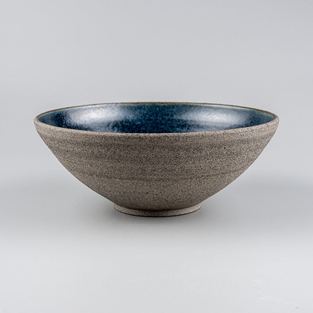 Side view of handmade stoneware bowl with unglazed rough-textured exterior and glazed blue interior.