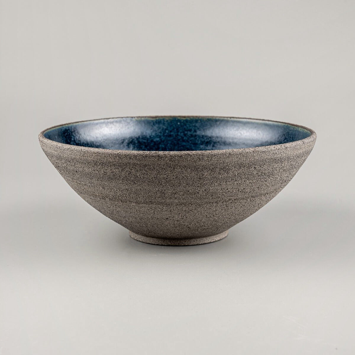 Side view of handmade stoneware bowl with unglazed rough-textured exterior and glazed blue interior.