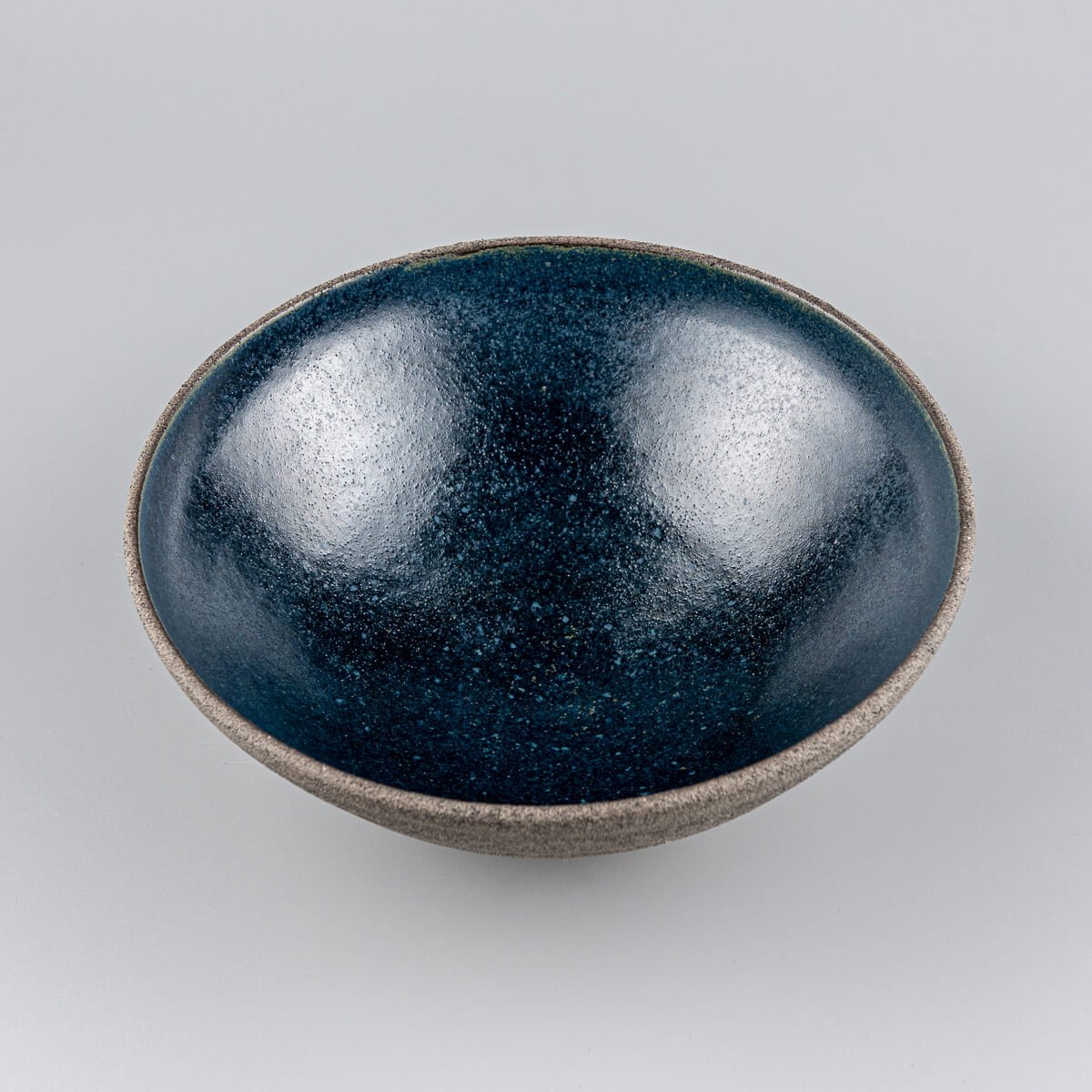 Angled front view of artisan-crafted bowl with contrasting raw clay surface and smooth glazed inside.