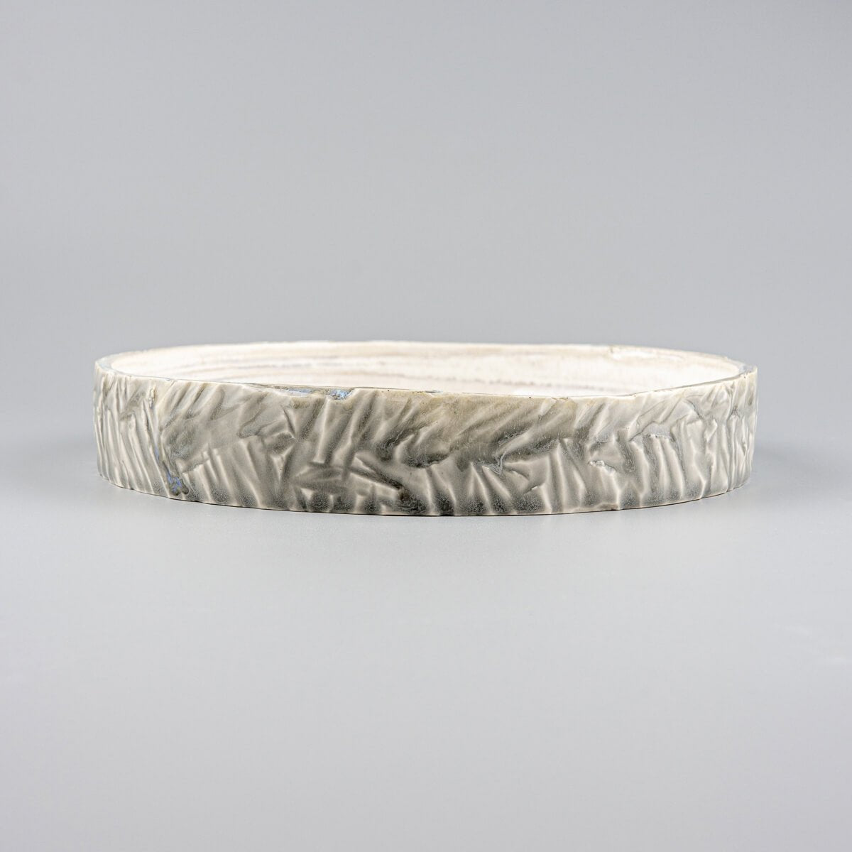 Close-up of handcrafted, unique ceramic plate with intricate carved outer edges and smooth glazed interior.