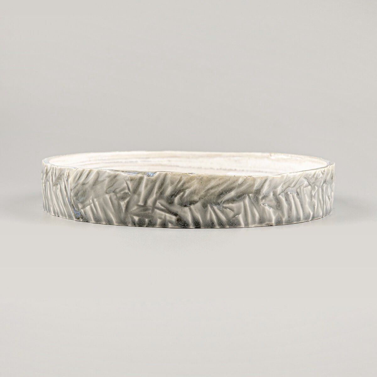 Close-up of handcrafted, unique ceramic plate with intricate carved outer edges and smooth glazed interior.