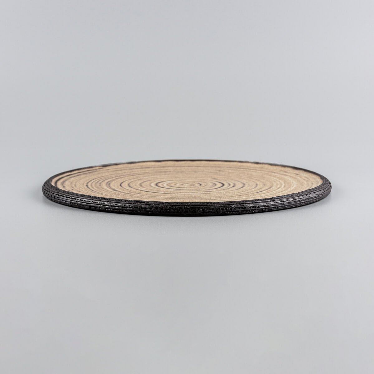 Elegant flat ceramic plate with ocher glazed surface and unglazed black clay rim.