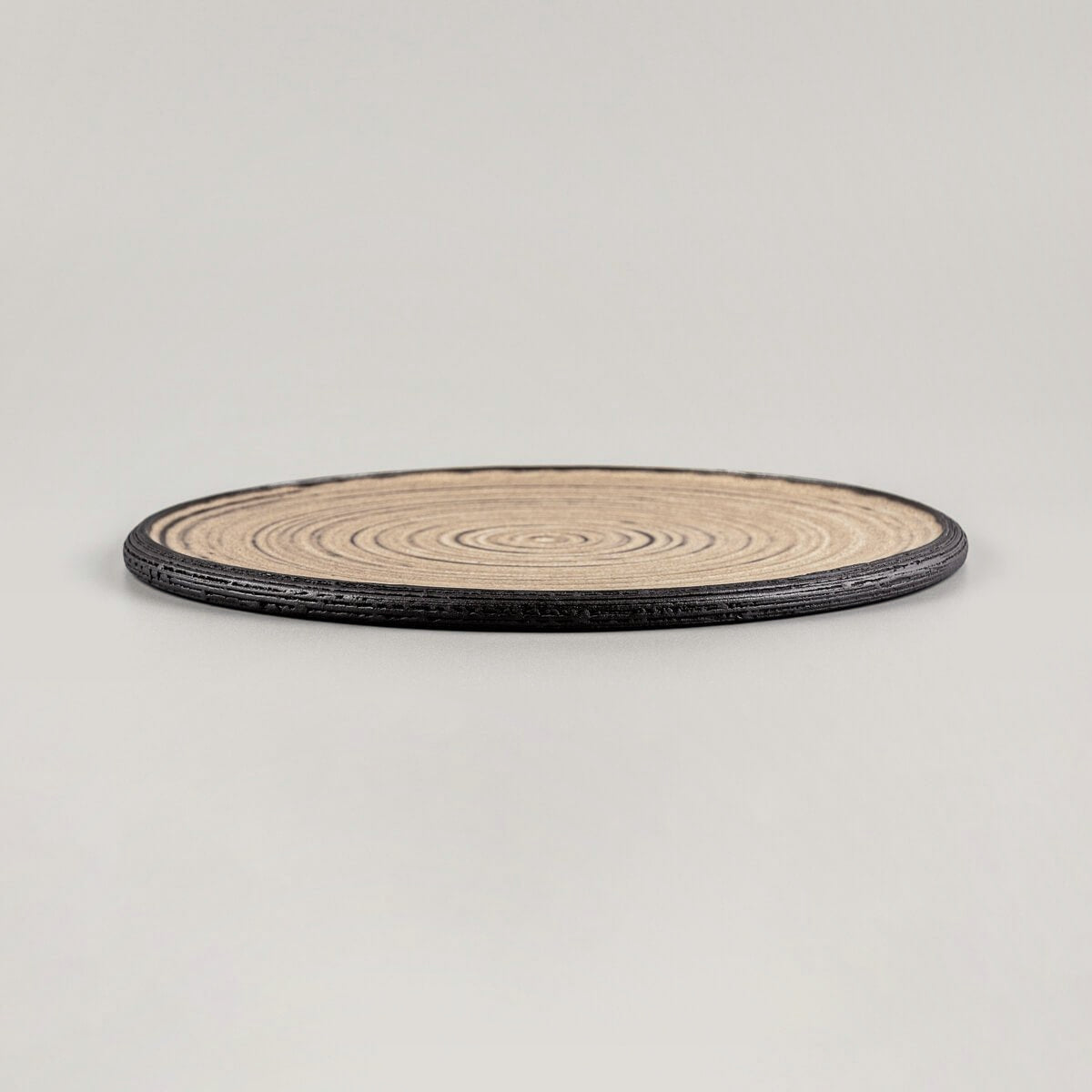 Elegant flat ceramic plate with ocher glazed surface and unglazed black clay rim.